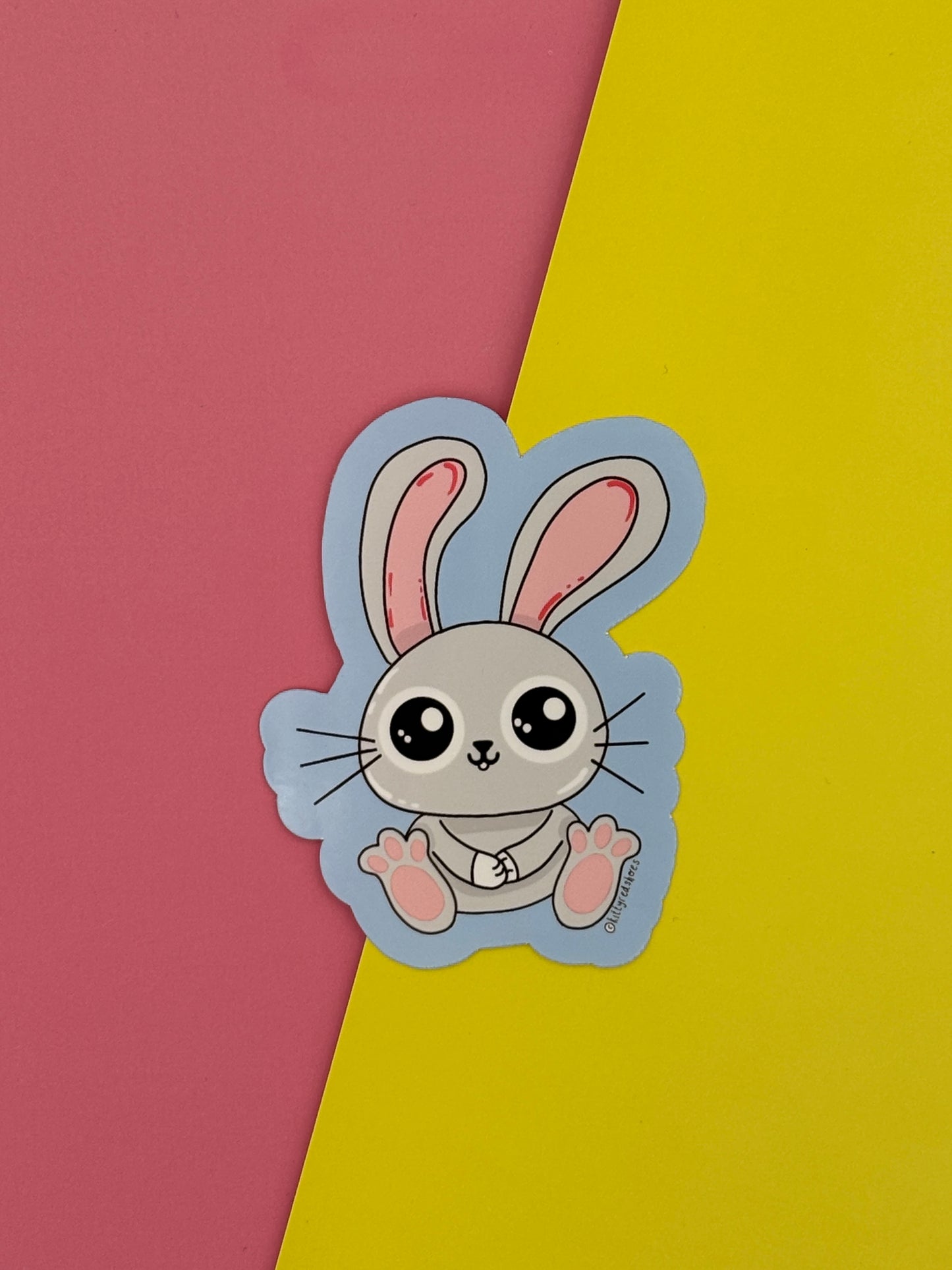 A sticker of a cute grey cartoon bunny with big ears on a blue background.