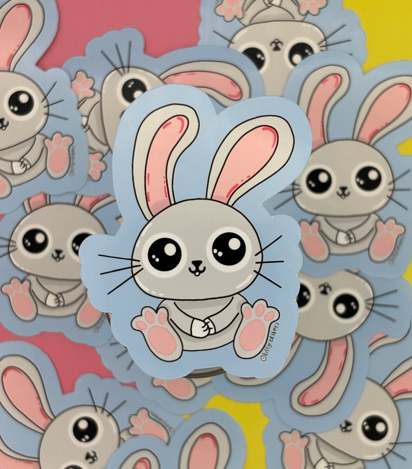 A sticker of a cute grey bunny with big ears on a blue background surrounded by many of the same sticker.