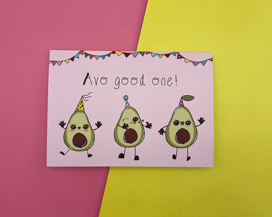 A pink greeting card with 3 cartoon avocados wearing party hats and the text: Avo good one! resting on a pink and yellow background. 