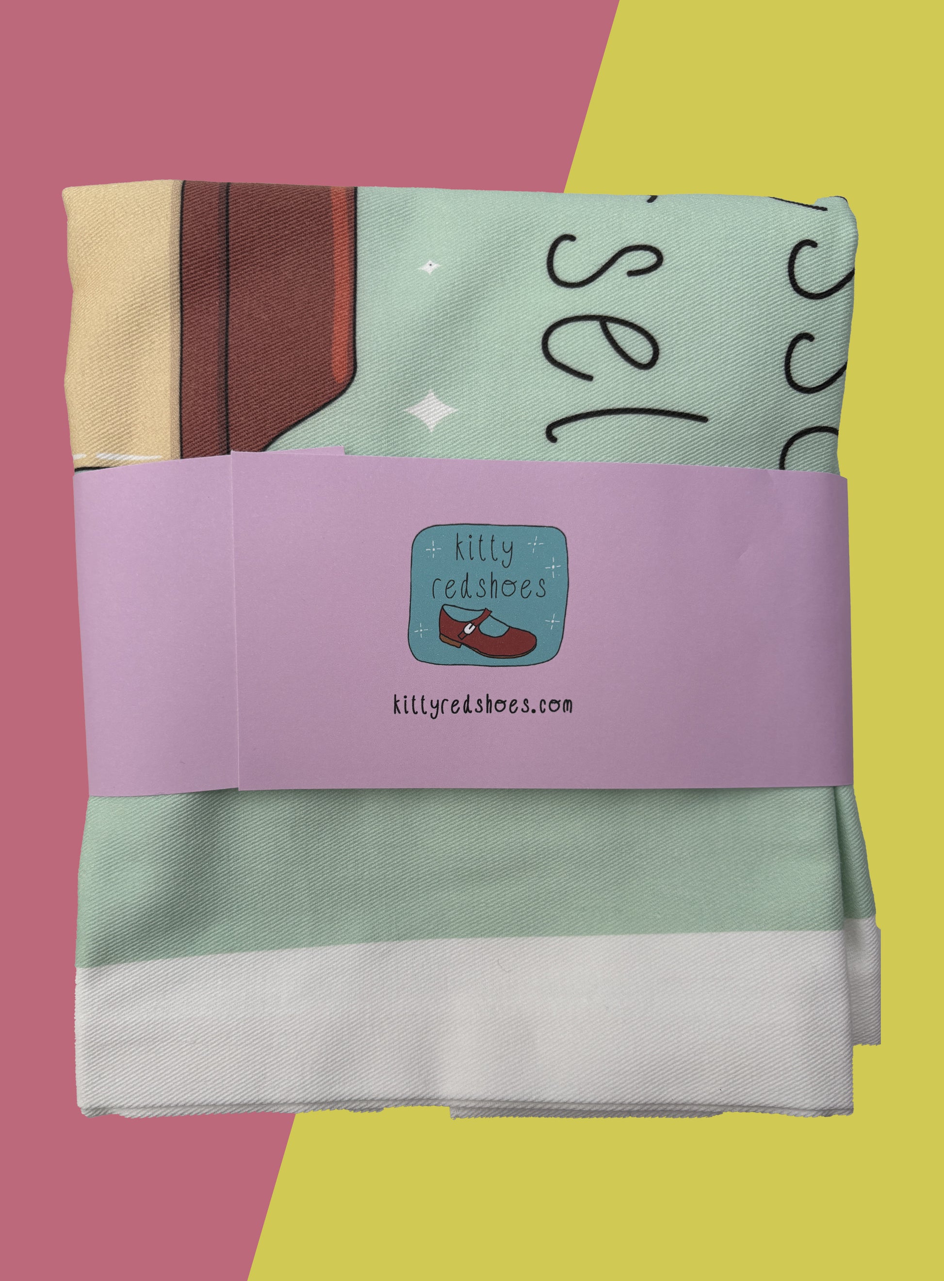 Back of folded coffee tote with purple belly band showing kitty redshoes logo and website.